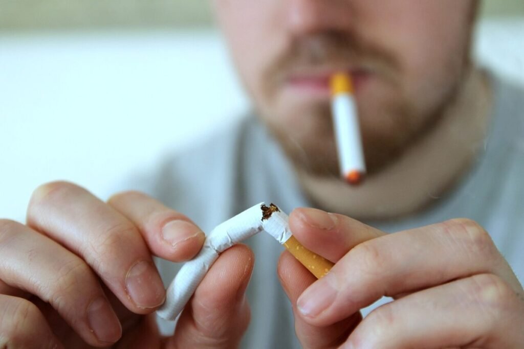 Mains cassant une cigarette en deux devant un homme flou, une autre cigarette aux lèvres