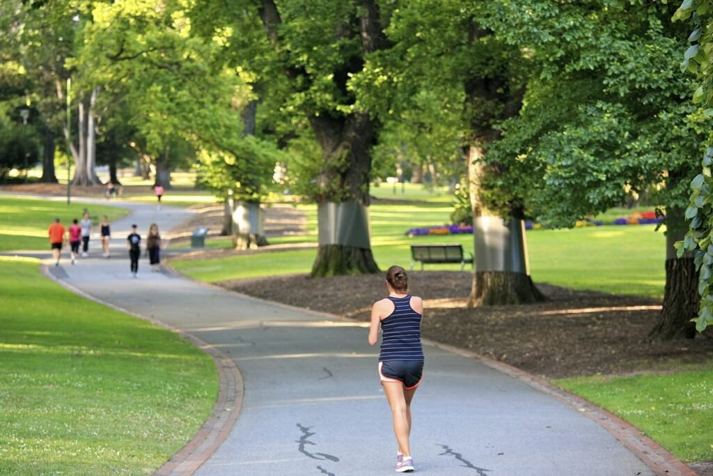 Joggeuse de dos sur une allée goudronnée d'un parc arboré, d'autres coureurs au loin