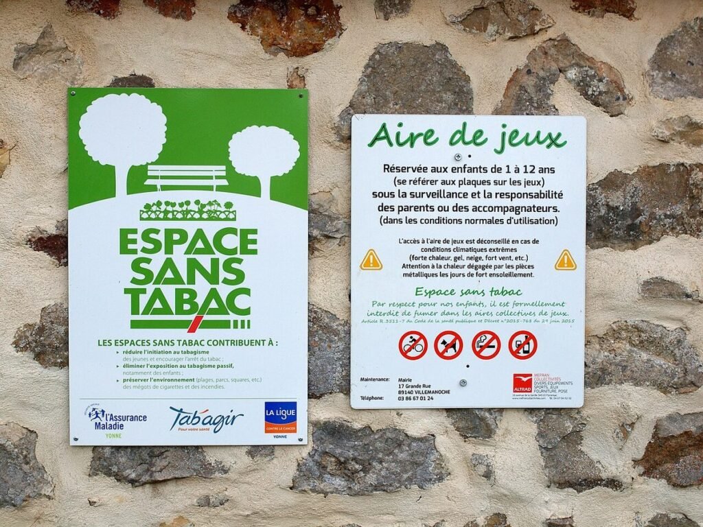 Panneaux « Espace sans tabac » et règlement d'une aire de jeux fixés sur un mur de pierre
