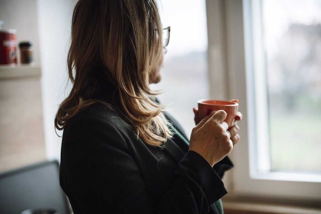 Femme pensive tenant une tasse de café devant une fenêtre de cuisine