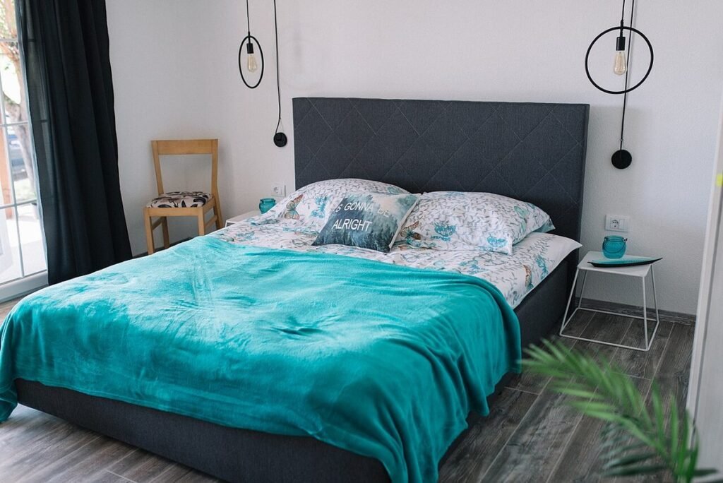 Chambre lumineuse avec un grand lit, une couverture turquoise et deux suspensions